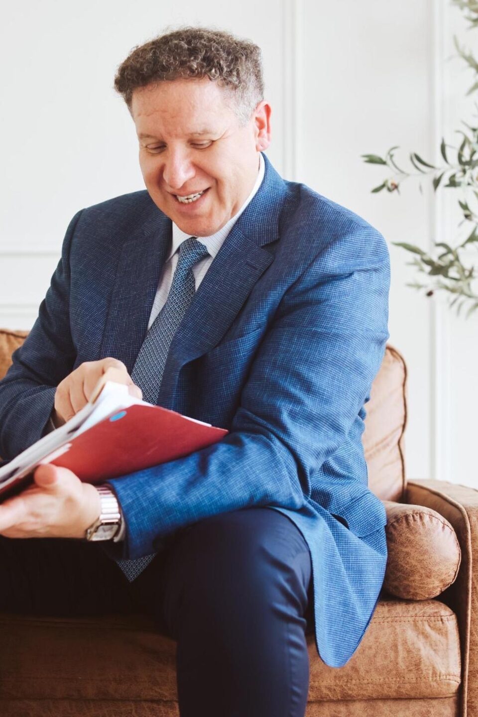 Attorney Carlos Maury reviewing a case file on a leather sofa.