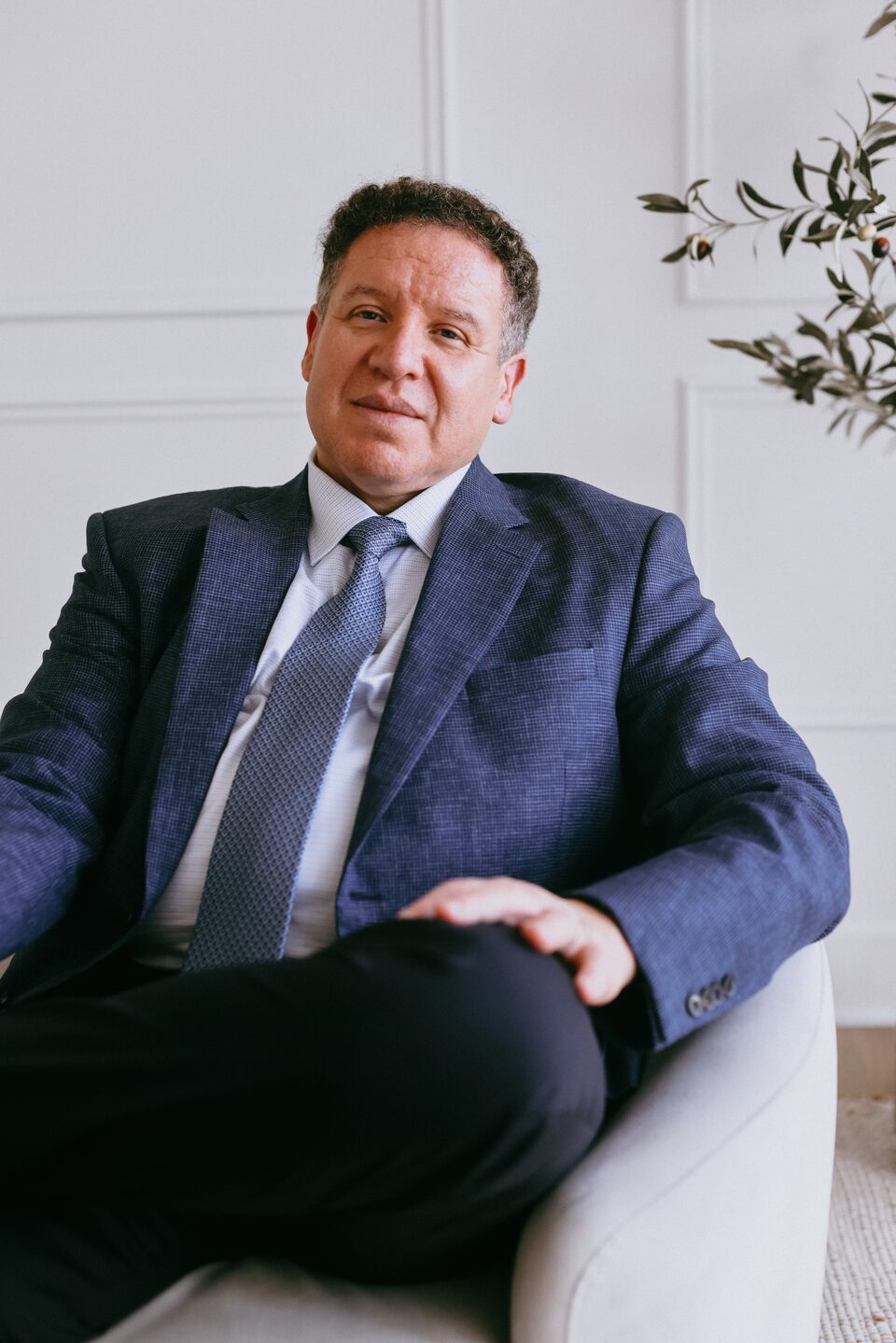 Attorney Carlos Maury, a former U.S. Immigration Judge, seated in a blue suit and tie.