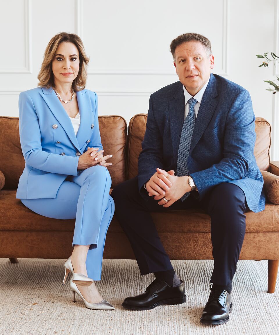 Immigration attorneys Erika Roman and Carlos Maury seated side by side on a sofa.